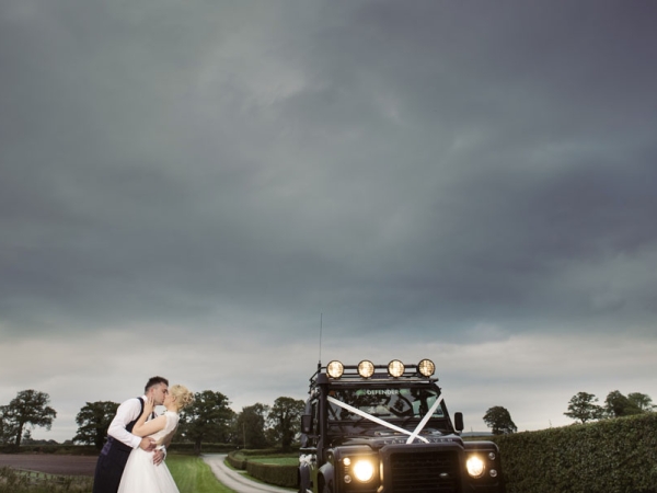 bride and groom kiss by land rover defender, cheshire wedding photographer, sandhole oak barn